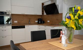 A modern kitchen with white cabinets and wooden accents. A vase with colorful flowers is on the table.