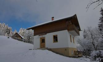 A beautiful house in the snow, surrounded by snowy trees. The sky is partly cloudy, creating a serene winter atmosphere.