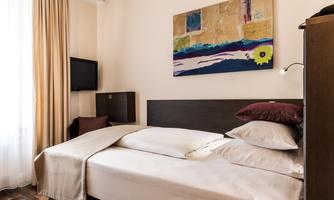 A cozy bedroom with a double bed and colorful artwork on the wall. The room is well-lit and has a television as well as curtains.