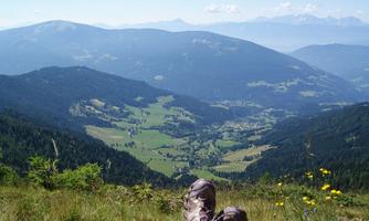A beautiful view of the valley from a mountain peak. The landscape is green with meadows and mountains in the background.