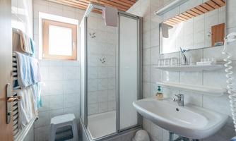 A modern bathroom with a shower and a sink. Towels hang on the wall and a window provides daylight.
