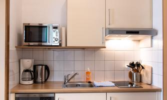 A modern kitchen with white cabinets and a wooden countertop. There is a stove, a microwave, a coffee machine, and a dishwasher.