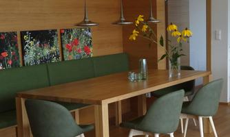 A modern dining room with a wooden table and green chairs. Pictures of flowers hang on the wall, and a vase with yellow flowers sits on the table.