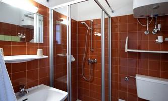 A modern bathroom with a shower-separating glass wall. The walls are tiled in warm terracotta tones and there is a sink and a toilet unit.