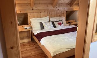 A cozy bedroom with a wooden bed and a red bedspread. The walls are made of wood and there is soft lighting.