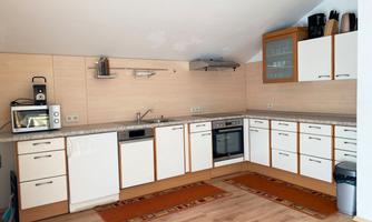 A modern kitchen with bright wooden surfaces and white cabinets. In the foreground, two rugs are on the floor.