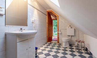 A modern bathroom with a white sink fixture and a toilet area. The floor is designed with black and white tiles, and a window leads outside.