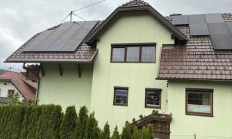 A modern house with a light green facade and a gable roof. Solar panels are installed on the roof.