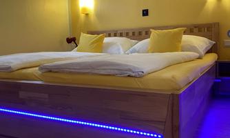A cozy bedroom with a double bed and yellow pillows. The distinctly modern lighting with blue LEDs creates a pleasant atmosphere.