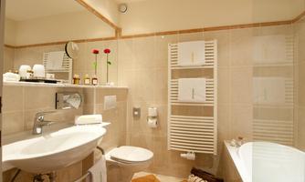 A modern bathroom with a bathtub and a sink. The walls are lightly tiled, and there are decorative elements such as flowers and towels.