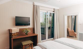A quiet bedroom with a double bed, a television, and a table. Large windows let in plenty of daylight, and there is a cozy armchair in the room.