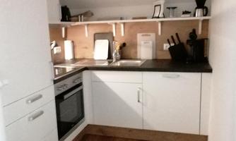 A modern kitchen with white cabinets and a black work area. On the countertop are various kitchen appliances and there is wooden flooring.