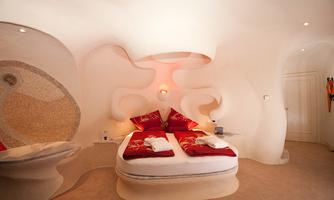 A modern bedroom with curved walls and red pillows. The soft lighting creates a pleasant atmosphere.
