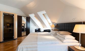 A modern bedroom with slanted windows and a large double bed. In the background, there is a sauna and stylish lighting.