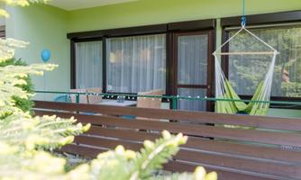 A balcony with a hammock and a bright, inviting interior. The green wall and the plants create a relaxed atmosphere.
