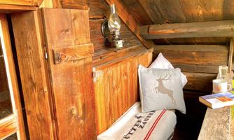 A cozy interior with wooden walls. On a bench lies a cushion, and a lamp provides warm light.