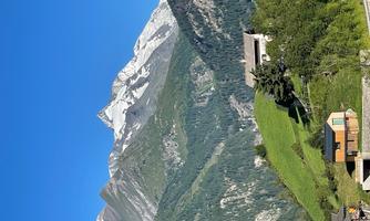 A picturesque mountain landscape with snow-capped peaks and lush green meadows. In the foreground, there are some traditional houses.
