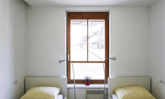A bright bedroom with two beds and yellow cushions. A large window with an outside view and a small plant on the windowsill.