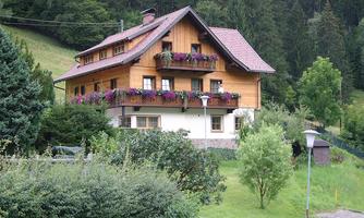 A charming house with a wooden facade and colorful flower boxes. Surrounded by green landscape and trees.