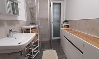 A modern bathroom with a shower and a sink. The space is bright and minimalist with wood and plant decorations.