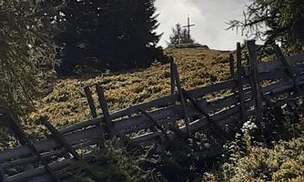 A picturesque landscape with a covered meadow and a wooden fence. In the background, a cross is visible among the trees.