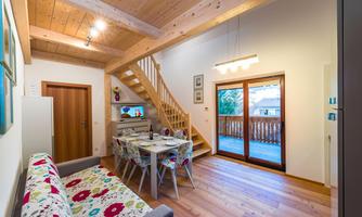 A cozy living space with a wooden ceiling and staircase. A dining table is next to a large window with access to the balcony.