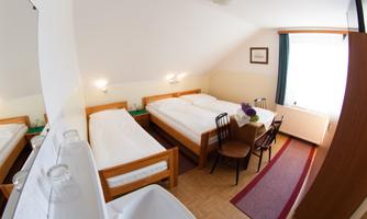 A cozy room with two beds and a table. The room has large windows and a friendly, bright atmosphere.