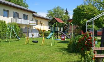 A beautiful playground with swings and slides on a green meadow. In the background, some houses and trees can be seen.