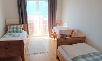 A bright room with two single beds and a table. Large windows let in plenty of daylight.