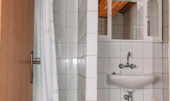 A simple bathroom with a shower, a sink, and a wooden ceiling. The walls are tiled with white tiles.