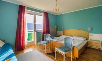 A cozy room with two beds, a table, and chairs. Through the windows, there is a beautiful view of the mountains.