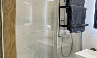 A modern shower with a glass partition and gray towels. The room has bright tiles and a minimalist design.