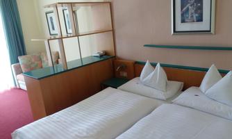 A cozy hotel room with two single beds and modern furniture. In the background, there is an armchair and a window that lets in plenty of light.