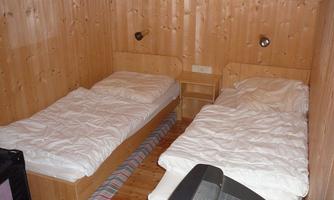 A simple room with two single beds and wooden paneling. The room is bright and cozily furnished.