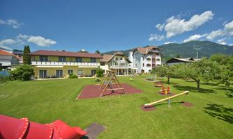 A large garden with playground equipment, including a slide and a swing. In the background, there are buildings and a clear blue sky.