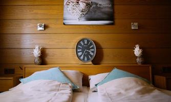 A cozy bedroom with a double bed and turquoise pillows. On the wall hangs a clock and a decorative picture.