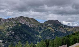An impressive mountain landscape with green forests and a cloudy sky. The mountains rise majestically in the background.