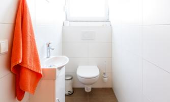 A modern bathroom with bright walls and a large window. An orange towel hangs on the wall next to a sink and a toilet.