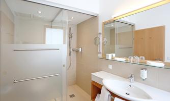 A modern bathroom with a glass shower and a large mirror. The walls are bright and the design is minimalist.