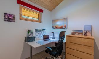 A modern office with a desk, a chair, and shelves. Pictures are hanging on the wall, and the window lets in a lot of light.