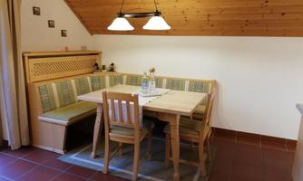 A cozy dining area with a wooden table and bench. The walls are clad in wood and the lighting is friendly.