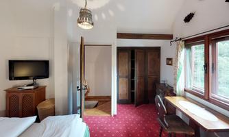 A cozy room with a beautiful view and a red carpet. It has a bed, a table, a television, and a wardrobe.