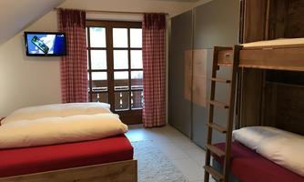 A cozy bedroom with a double bed and a bunk bed. A TV is mounted on the wall and large windows provide plenty of light.