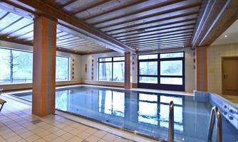 A modern indoor swimming pool with large windows and a wooden ceiling. The water is clear and inviting, surrounded by a tranquil ambiance.