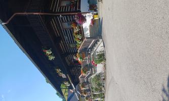 A traditional wooden house with flowers in boxes and a generous staircase. The sky is clear and it is sunny.