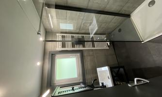 A modern bathroom with a glass shower and a sink. The walls are in a gray tone and there is plenty of natural light from a window.