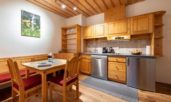 A cozy kitchen with wooden furniture and a table. The walls are light and a small piece of artwork hangs on the wall.