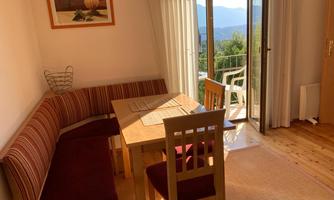 An inviting dining area with a table and chairs. Large windows offer a view of the nature outside.
