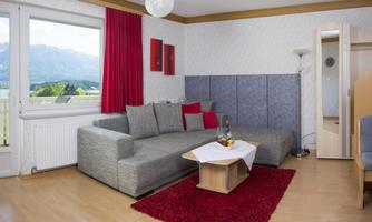 Cozy living space with a gray sofa and a red carpet. Large window view of the mountains and bright colors create an inviting atmosphere.