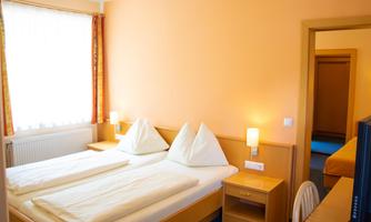 A cozy hotel room with two beds and a bright, inviting atmosphere. The walls are painted orange, and there are windows with plenty of natural light.